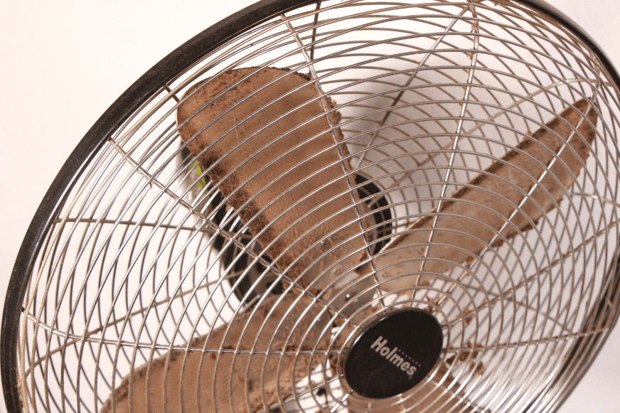 An den Rotorblättern eines Standventilators hängen Staubklumpen